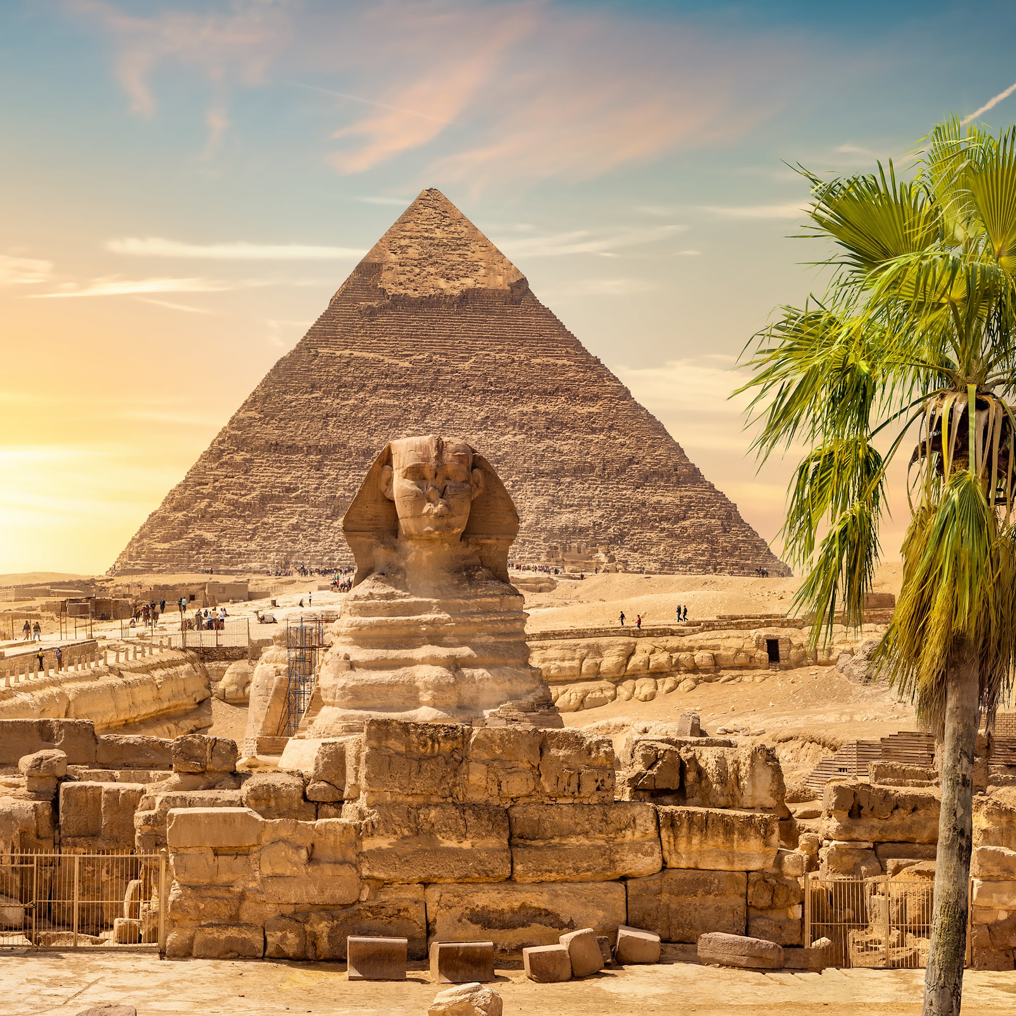 The Great Pyramid and Sphinx of Giza at sunset with palm trees and tourists exploring Egypt’s iconic landmarks.